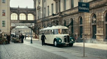 Movie still from “Never Look Away” (2018), directed by Florian Henckel von Donnersmarck – A man walking down the street in front of a bus; Extreme Wide shot, High angle