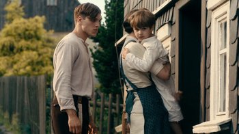 Movie still from “Never Look Away” (2018), directed by Florian Henckel von Donnersmarck – A man and a woman holding each other while another man looks on; Medium shot, Over the shoulder angle