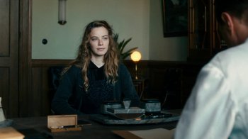 Movie still from “Never Look Away” (2018), directed by Florian Henckel von Donnersmarck – A woman sitting at a table in front of a lamp; Medium shot, Over the shoulder angle