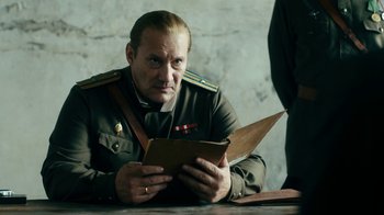 Movie still from “Never Look Away” (2018), directed by Florian Henckel von Donnersmarck – A man in uniform sitting at a table reading a book; Medium shot, Over the shoulder angle