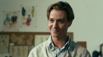 Movie still from “Never Look Away” (2018), directed by Florian Henckel von Donnersmarck – A young man smiling for the camera in a room; Close Up shot, Over the shoulder angle