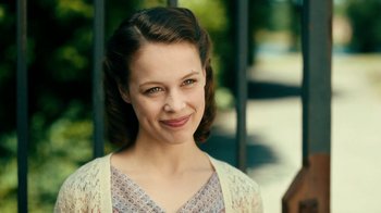 Movie still from “Never Look Away” (2018), directed by Florian Henckel von Donnersmarck – A young woman with blue eyes smiles for the camera; Close Up shot, Over the shoulder angle