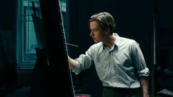 Movie still from “Never Look Away” (2018), directed by Florian Henckel von Donnersmarck – A man painting a picture on an easel in a dark room; Medium shot, Low angle