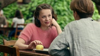 Movie still from “Never Look Away” (2018), directed by Florian Henckel von Donnersmarck – A woman sitting next to a man at a table with an apple in front of her; Close Up shot, Over the shoulder angle