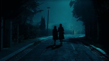 Movie still from “Never Look Away” (2018), directed by Florian Henckel von Donnersmarck – Two people walking down a street at night; Extreme Wide shot, Low angle