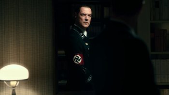Movie still from “Never Look Away” (2018), directed by Florian Henckel von Donnersmarck – A man in a nazi uniform standing in front of a bookshelf; Medium shot, Over the shoulder angle