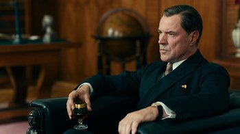 Movie still from “Never Look Away” (2018), directed by Florian Henckel von Donnersmarck – A man sitting in a chair holding a glass of wine; Medium shot, Over the shoulder angle