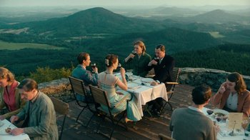 Movie still from “Never Look Away” (2018), directed by Florian Henckel von Donnersmarck – A group of people sitting at a table with mountains in the background; Wide shot, High angle