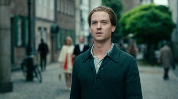 Movie still from “Never Look Away” (2018), directed by Florian Henckel von Donnersmarck – A man in a green jacket standing on the sidewalk; Close Up shot, Low angle