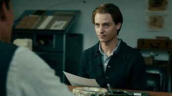 Movie still from “Never Look Away” (2018), directed by Florian Henckel von Donnersmarck – A man sitting at a table holding a piece of paper; Close Up shot, Over the shoulder angle