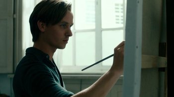 Movie still from “Never Look Away” (2018), directed by Florian Henckel von Donnersmarck – A young man holding a brush and painting on a wall; Close Up shot, Low angle