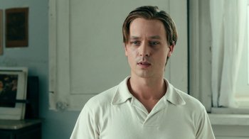 Movie still from “Never Look Away” (2018), directed by Florian Henckel von Donnersmarck – A man in a white shirt is standing in a room; Close Up shot, Low angle