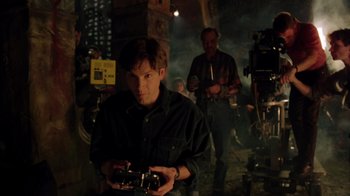 Movie still from “New Nightmare” (1994), directed by Wes Craven – A man holding a camera in front of a camera crew; Medium shot, High angle