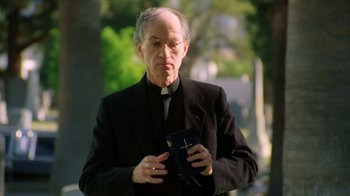 Movie still from “New Nightmare” (1994), directed by Wes Craven – An older man holding a bible while wearing glasses; Medium shot, Low angle