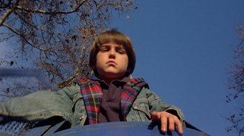 Movie still from “New Nightmare” (1994), directed by Wes Craven – A young boy is sitting on a blue slide; Close Up shot, Low angle