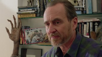 Movie still from “New Nightmare” (1994), directed by Wes Craven – A person in a room with books; Close Up shot, Over the shoulder angle