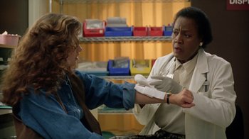 Movie still from “New Nightmare” (1994), directed by Wes Craven – A woman getting her arm examined by a doctor; Medium shot, Over the shoulder angle