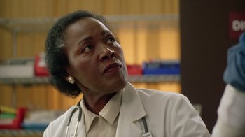 Movie still from “New Nightmare” (1994), directed by Wes Craven – An older woman wearing a white lab coat and stethoscope; Close Up shot, Low angle