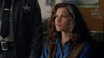 Movie still from “New Nightmare” (1994), directed by Wes Craven – A woman with long brown curly hair sitting in front of a police officer; Close Up shot, Over the shoulder angle
