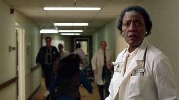 Movie still from “New Nightmare” (1994), directed by Wes Craven – A woman wearing a white lab coat in a hospital hallway; Medium shot, Low angle