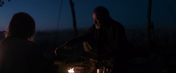 Movie still from “News of the World” (2020), directed by Paul Greengrass – A man is lighting a fire at night time; Medium shot, Over the shoulder angle