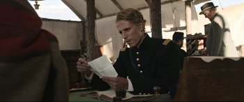 Movie still from “News of the World” (2020), directed by Paul Greengrass – A man sitting at a table holding a piece of paper; Medium shot, Over the shoulder angle