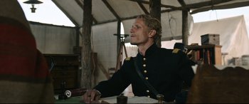 Movie still from “News of the World” (2020), directed by Paul Greengrass – A man in a military uniform sitting at a table; Medium shot, Low angle