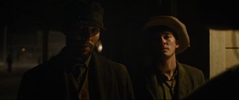 Movie still from “News of the World” (2020), directed by Paul Greengrass – Two men standing next to each other in the dark; Medium shot, Low angle