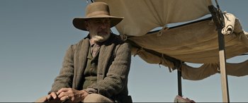 Movie still from “News of the World” (2020), directed by Paul Greengrass – An old man with a beard and a hat sitting under an awning; Medium shot, Over the shoulder angle