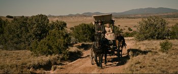 Movie still from “News of the World” (2020), directed by Paul Greengrass – A man and a woman riding in a horse drawn carriage down a dirt road; Wide shot, High angle