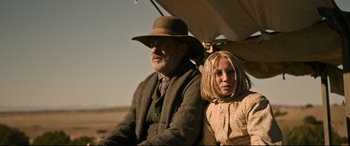 Movie still from “News of the World” (2020), directed by Paul Greengrass – An older man and a young woman sitting next to each other; Medium shot, Low angle