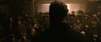 Movie still from “News of the World” (2020), directed by Paul Greengrass – A group of people in a room with a man in the foreground; Medium shot, Over the shoulder angle