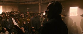 Movie still from “News of the World” (2020), directed by Paul Greengrass – A man with a long beard standing in front of a group of people; Medium shot, Over the shoulder angle