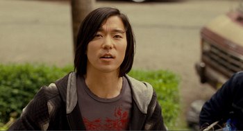 Movie still from “Nick and Norah's Infinite Playlist” (2008), directed by Peter Sollett – A man with long black hair wearing a gray t - shirt; Close Up shot, Over the shoulder angle