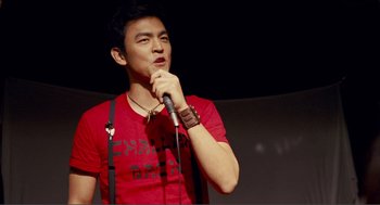 Movie still from “Nick and Norah's Infinite Playlist” (2008), directed by Peter Sollett – A man in red shirt holding a microphone; Medium shot, Over the shoulder angle