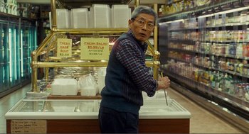 Movie still from “Nick and Norah's Infinite Playlist” (2008), directed by Peter Sollett – An older man holding a knife in a grocery store; Medium shot, Over the shoulder angle