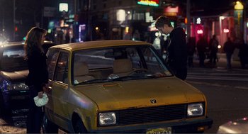 Movie still from “Nick and Norah's Infinite Playlist” (2008), directed by Peter Sollett – A man standing next to a yellow car on the street; Wide shot, Over the shoulder angle