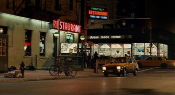 Movie still from “Nick and Norah's Infinite Playlist” (2008), directed by Peter Sollett – A yellow taxi driving down a street next to a restaurant; Wide shot, High angle