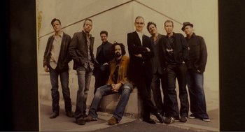 Movie still from “Nick and Norah's Infinite Playlist” (2008), directed by Peter Sollett – A group of men standing next to each other on a sidewalk; Medium shot, Low angle