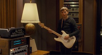 Movie still from “Nick and Norah's Infinite Playlist” (2008), directed by Peter Sollett – A young man holding a white guitar in a room; Medium shot, High angle