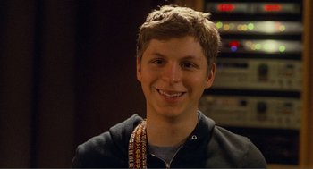 Movie still from “Nick and Norah's Infinite Playlist” (2008), directed by Peter Sollett – A young man smiling for the camera in front of a sound board; Close Up shot, Over the shoulder angle