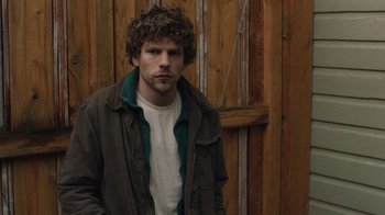 Movie still from “Night Moves” (2013), directed by Kelly Reichardt – A man standing in front of a wooden wall; Medium shot, Low angle
