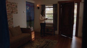 Movie still from “Night Moves” (2013), directed by Kelly Reichardt – A woman standing in front of a window in a living room; Wide shot, Over the shoulder angle