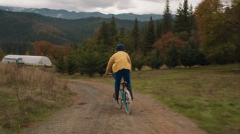 Movie still from “Night Moves” (2013), directed by Kelly Reichardt – A man riding a bike down a dirt road; Extreme Wide shot, High angle