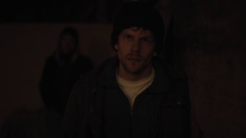 Movie still from “Night Moves” (2013), directed by Kelly Reichardt – A man in a black jacket and a black hat is in the dark; Close Up shot, Over the shoulder angle