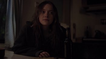 Movie still from “Night Moves” (2013), directed by Kelly Reichardt – A woman sitting at a table with a bottle of beer; Medium shot, Over the shoulder angle