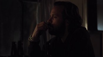 Movie still from “Night Moves” (2013), directed by Kelly Reichardt – A man with long hair and a beard sitting in a dark room; Close Up shot, Over the shoulder angle