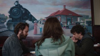 Movie still from “Night Moves” (2013), directed by Kelly Reichardt – A group of people sitting at a table in front of a painting; Medium shot, Over the shoulder angle