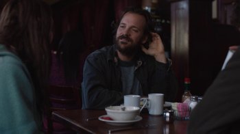 Movie still from “Night Moves” (2013), directed by Kelly Reichardt – A man sitting at a table with a cup of coffee; Medium shot, Over the shoulder angle