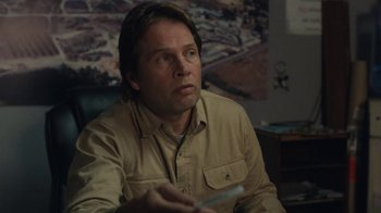 Movie still from “Night Moves” (2013), directed by Kelly Reichardt – A man sitting in a living room holding a remote control; Close Up shot, Over the shoulder angle